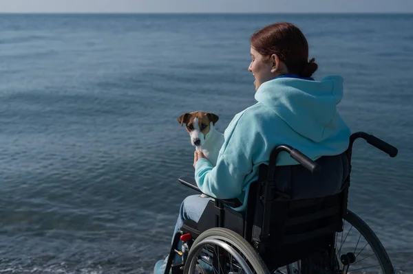 Vit kvinna i rullstol med hund vid havet. — Stockfoto