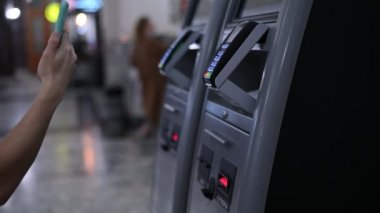 Bir kadın tren bileti almak için self-servis kasasında cep telefonuyla ödeme yapar.. 