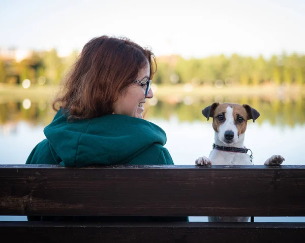 白人女性は湖のそばの犬とベンチに座っている. — ストック写真