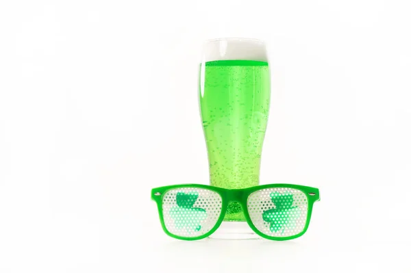 Un verre de bière verte et des verres drôles pour la journée st patricks sur fond blanc. Boisson traditionnelle irlandaise pour des vacances. Copier spase. — Photo