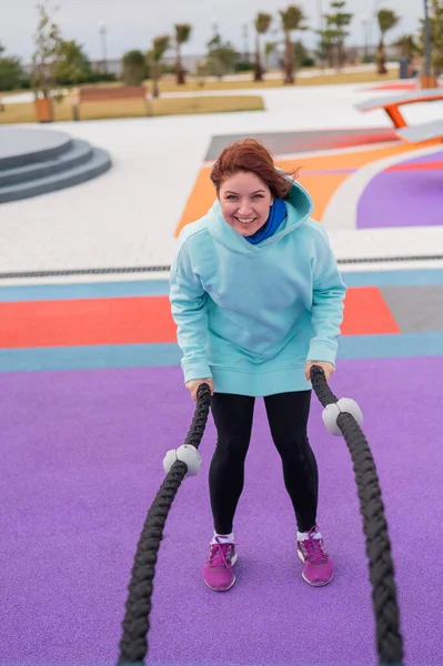 Kaukasierin im Mint-Sweatshirt trainiert am Sportplatz mit Kampfleinen. — Stockfoto