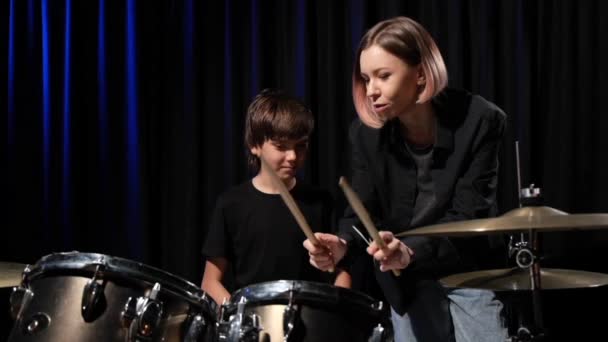 Jeune femme caucasienne enseigne à un garçon à jouer de la batterie dans le studio sur un fond noir. Étudiant en musique — Video