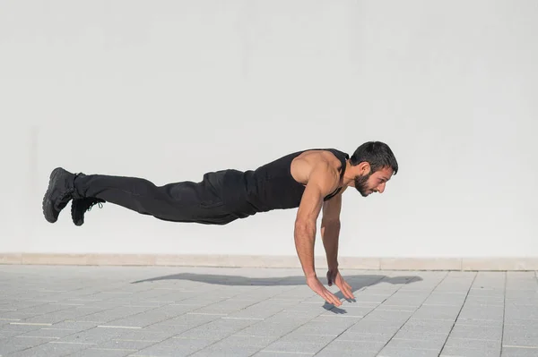 A man in black sportswear jumps while doing push-ups outdoors.