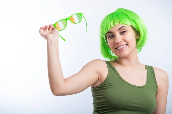 Веселая молодая женщина в зеленом парике и смешных очках празднует День святого Патрика на белом фоне — стоковое фото