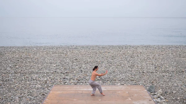 Homme caucasien avec torse nu pratiquant wushu sur le bord de la mer. — Photo