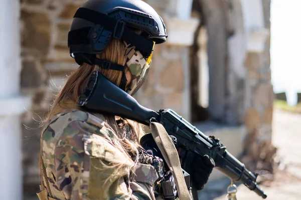 Mujer caucásica en traje protector con ametralladora. Una soldado con uniforme de camuflaje sostiene un arma. — Foto de Stock