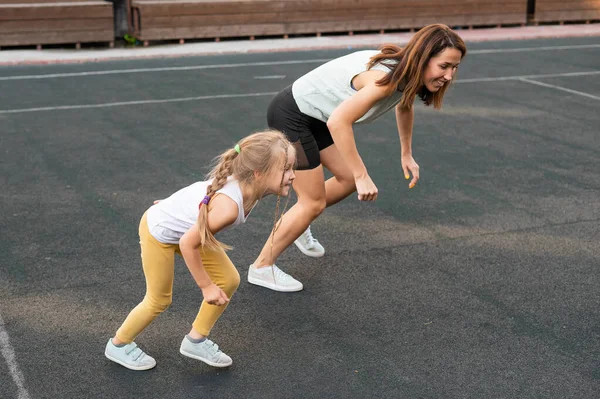 Běloška chodí ven na sport se svou dcerou. Na stadionu pobíhá školačka a její matka.. — Stock fotografie