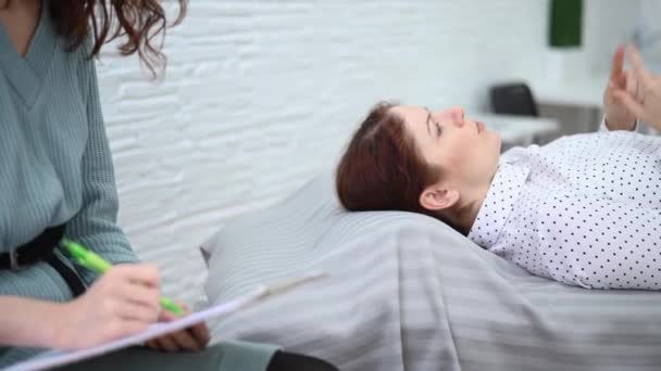 Кавказская женщина лежит на диване и выражает свои чувства, в то время как психолог делает записи на планшете. — стоковое видео
