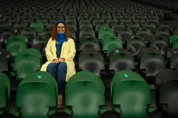 Vit kvinna hejar på ett idrottslag på stadion. Flickan tittar på matchen på arenan ensam. — Stockfoto