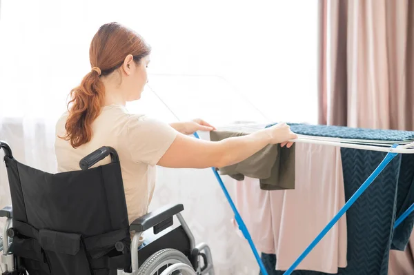 Mulher branca em uma cadeira de rodas pendura roupa molhada em um secador. — Fotografia de Stock