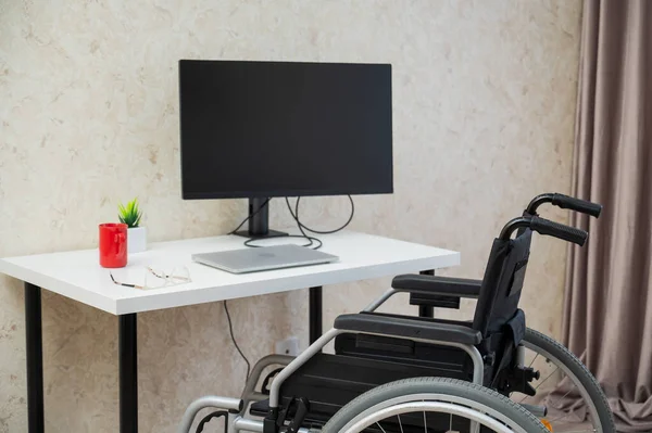 Miejsce pracy dla osoby niepełnosprawnej. Wózek inwalidzki przy stole z komputerem. — Zdjęcie stockowe