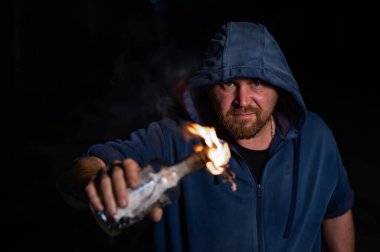 Kapüşonlu adam yanan bir şişe tutuyor. Molotof kokteyli.