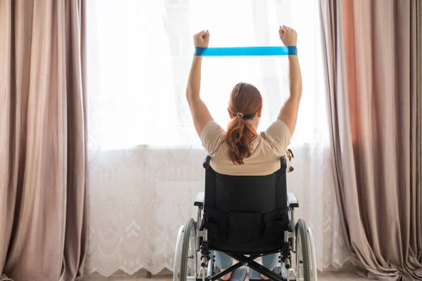 Blanke vrouw in een rolstoel doet oefeningen met behulp van fitness elastiekjes. — Stockfoto