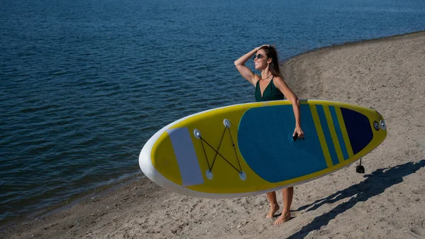 Kaukasische Frau spaziert am Strand entlang und trägt ein Surfbrett auf dem Fluss in der Stadt. Sommersport. — Stockfoto