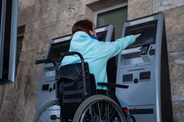 Tekerlekli sandalyedeki beyaz bir kadın tren istasyonundaki self servis kasasına ulaşamaz. Ulaşılması zor bir ortam.