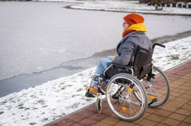 Tekerlekli sandalyedeki beyaz kadın kışın gölün kenarında yürür..