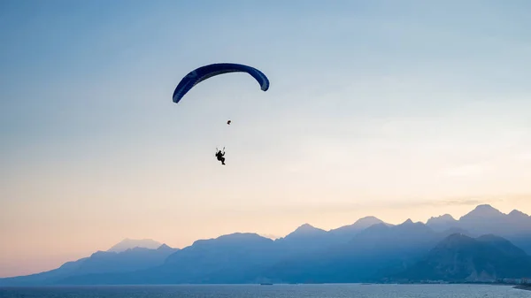 Silhueta de um homem em um parapente voando sobre o mar ao pôr do sol. — Fotografia de Stock