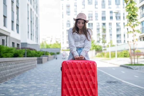 Schöne kaukasische brünette Frau mit Hut posiert mit einem Koffer auf einer Straße der Stadt. — Stockfoto