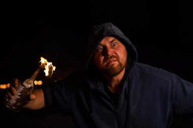 Kapüşonlu adam yanan bir şişe tutuyor. Molotof kokteyli.