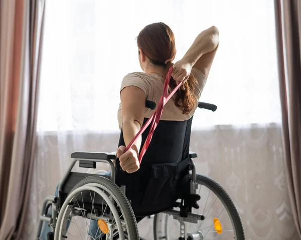 Caucasian woman in a wheelchair doing exercises with the help of fitness rubber bands.