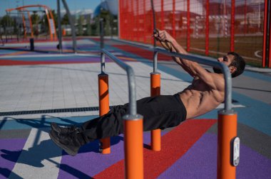 Spor sahasındaki paralel çubuklarda üstsüz adam yatay denge yapıyor.. 