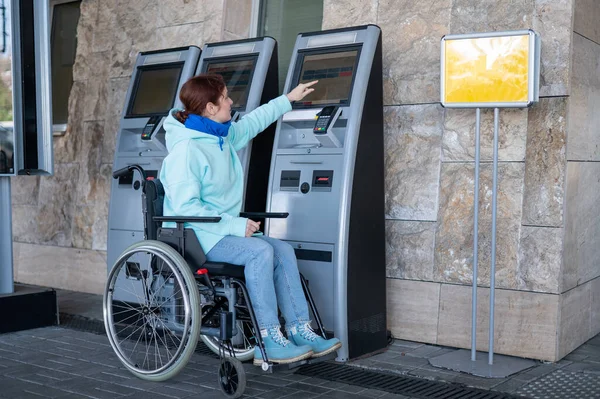 Белая женщина в инвалидной коляске покупает билет на поезд на кассе самообслуживания. — стоковое фото