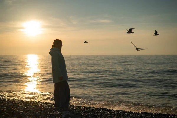Donna caucasica che nutre gabbiani al tramonto in riva al mare. — Foto Stock