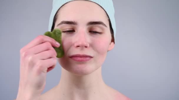 Närbild porträtt av en ung kvinna massera hennes ansikte med en gouache skrapa. — Stockvideo
