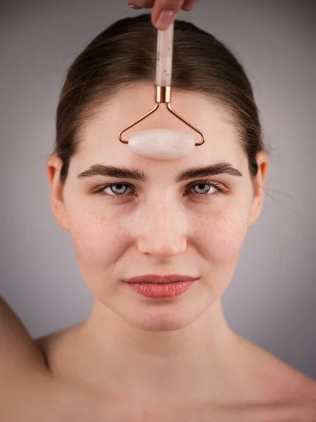 Retrato de cerca de una mujer utiliza un masajeador de rodillos de cuarzo para suavizar las arrugas en la frente. — Foto de Stock