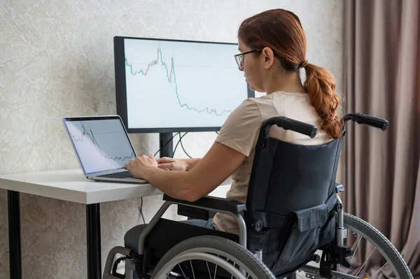 Mulher branca em uma cadeira de rodas digitando com um laptop de casa. Trabalho remoto para pessoas com deficiência. — Fotografia de Stock