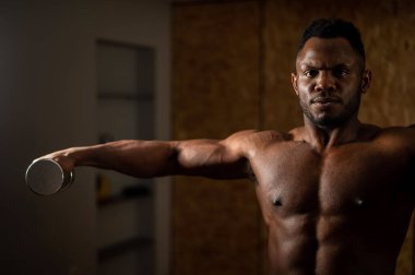 Çekici Afrikalı Amerikalı adam dambıllarla kol egzersizi yapıyor.. 