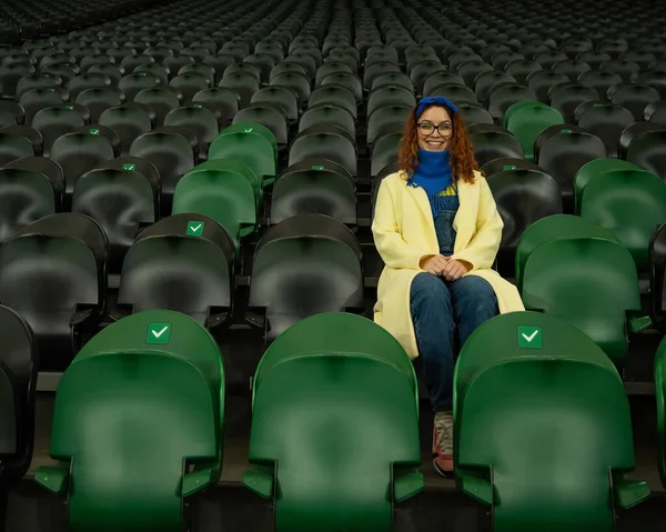 Vit kvinna hejar på ett idrottslag på stadion. Flickan tittar på matchen på arenan ensam. — Stockfoto