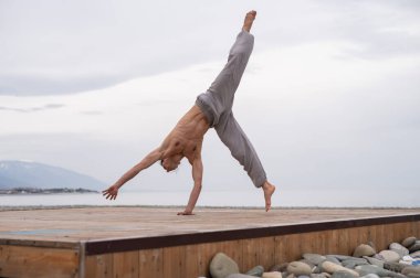 Üstsüz beyaz adam sahilde akrobatik tekerlek yapıyor.. 