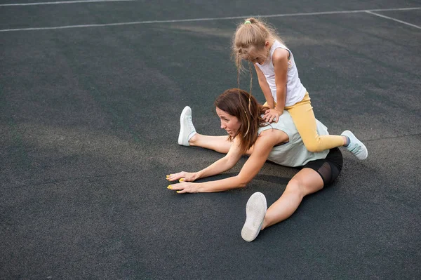 Mor och dotter går in för sport utomhus. Kaukasiska kvinna och liten flicka är engagerade i kondition på stadion. — Stockfoto