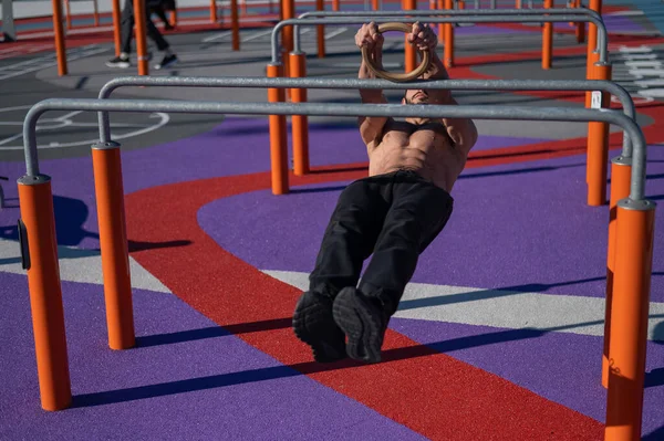 Shirtless mand gør vandret balance på parallelle barer på sportspladsen. - Stock-foto