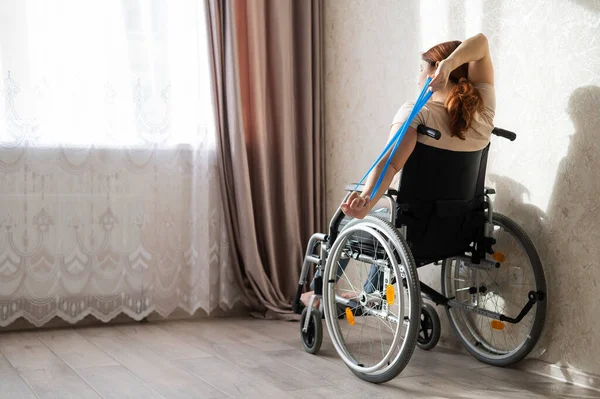 Blanke vrouw in een rolstoel doet oefeningen met behulp van fitness elastiekjes. — Stockfoto