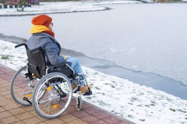 Tekerlekli sandalyedeki beyaz kadın kışın gölün kenarında yürür..