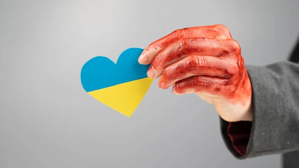 Femme avec les mains couvertes de sang tenant un cœur avec le drapeau de l'ukraine sur un fond blanc. — Photo