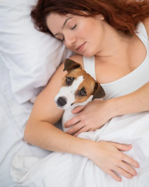 Mulher caucasiana está cochilando na cama abraçando seu cão amado. — Fotografia de Stock