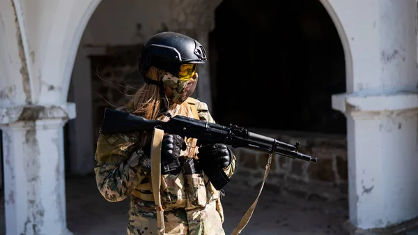 Mulher branca num fato de protecção com uma metralhadora. Uma soldado de uniforme de camuflagem segura uma arma.. — Fotografia de Stock