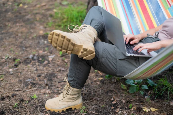 Mulher caucasiana trabalhando em laptop enquanto sentada em uma rede na floresta. Menina usa um computador sem fio em uma caminhada. — Fotografia de Stock