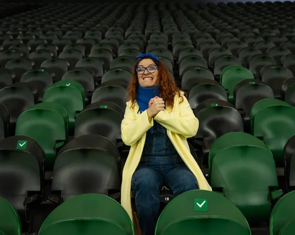 Vit kvinna hejar på ett idrottslag på stadion. Flickan tittar på matchen på arenan ensam. — Stockfoto