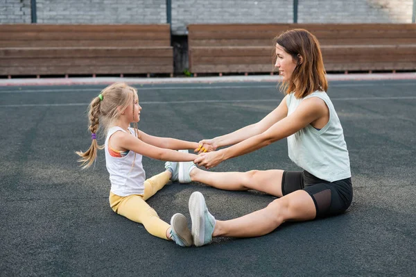 Мать и дочь занимаются спортом на свежем воздухе. Кавказка и девочка занимаются фитнесом на стадионе. — стоковое фото