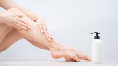 Kadın beyaz arka planda bacaklarına nemlendirici sürüyor. Kız cildine özen gösterir ve krem kullanır..