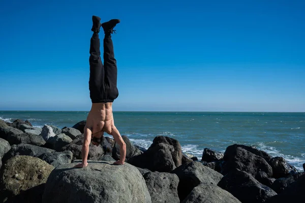 Ατρόμητος άντρας κάνει κατακόρυφο σε βράχους δίπλα στη θάλασσα. — Φωτογραφία Αρχείου