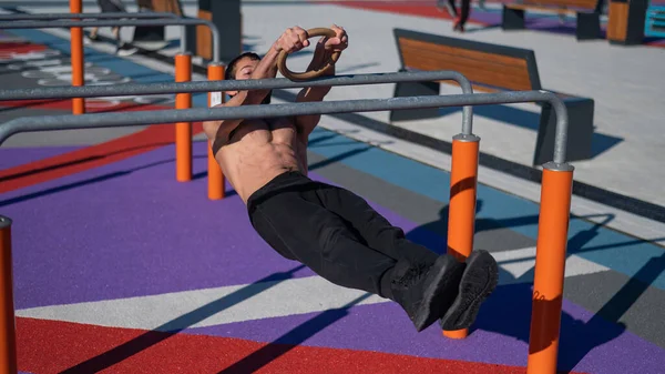 Uomo senza maglietta che fa equilibrio orizzontale su barre parallele al campo sportivo. — Foto Stock