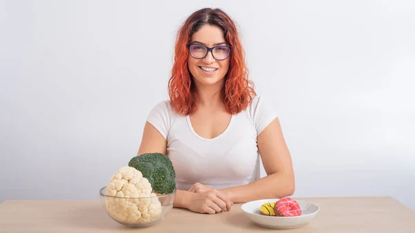Kaukasiska kvinnor föredrar hälsosam mat. rödhårig flicka väljer mellan broccoli och munkar på vit bakgrund. — Stockfoto