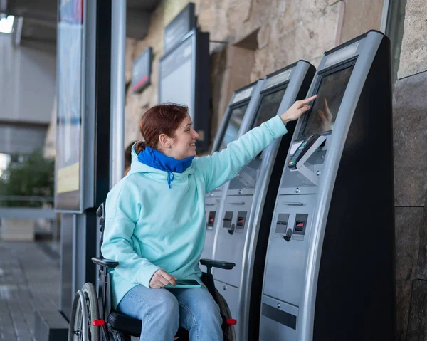 Tekerlekli sandalyedeki beyaz kadın self-servis kasasından tren bileti alıyor.. 