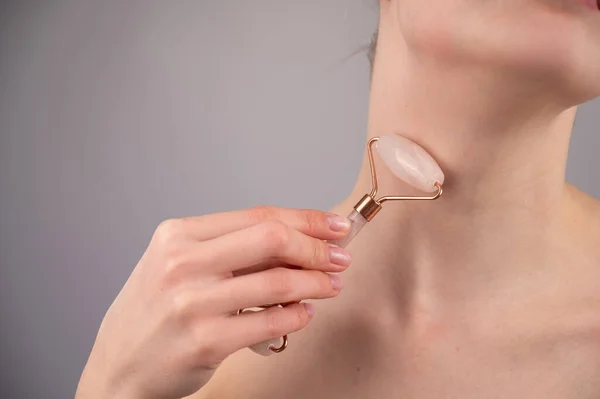 Close-up portrait of a woman using a quartz roller massager for an alternative fight against wrinkles on her neck. Smoothing of the rings of venus.