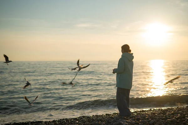Femme blanche nourrissant les mouettes au coucher du soleil au bord de la mer. — Photo